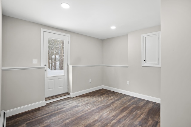 empty room with baseboard heating and dark hardwood / wood-style flooring