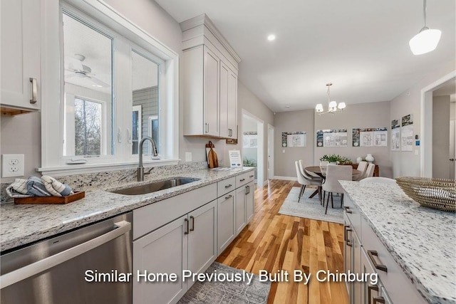 kitchen featuring decorative light fixtures, dishwasher, sink, light stone counters, and light wood-type flooring