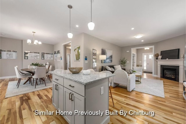 kitchen with a kitchen bar, light wood-type flooring, a kitchen island, pendant lighting, and light stone countertops