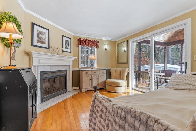 bedroom with ornamental molding, light wood-type flooring, a tile fireplace, and access to outside