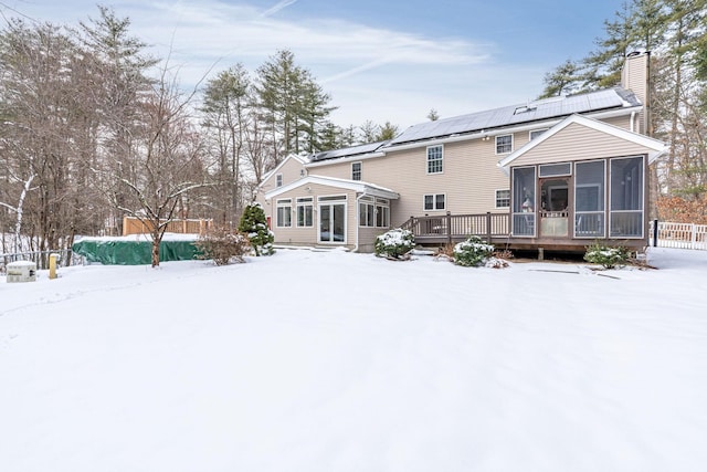 snow covered property with a wooden deck, a sunroom, and solar panels