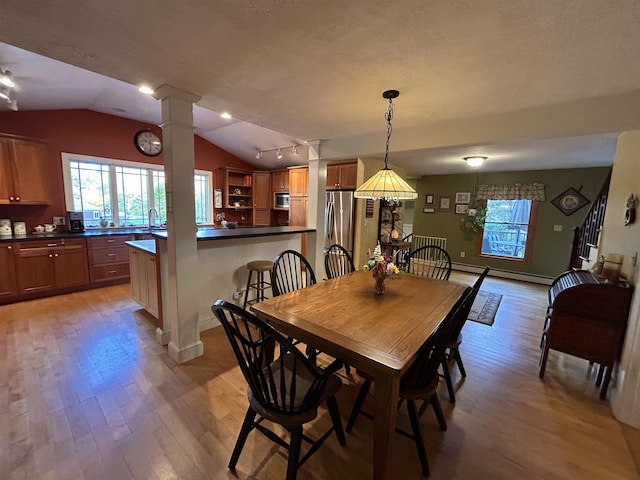 dining area featuring vaulted ceiling, a baseboard heating unit, light hardwood / wood-style floors, and ornate columns