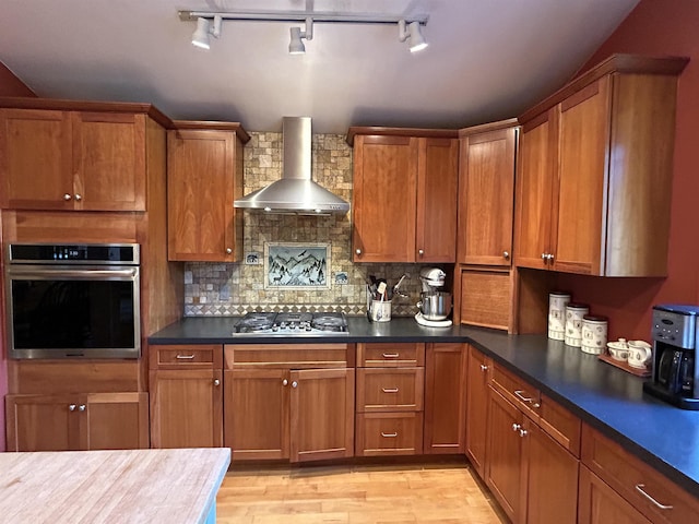 kitchen with stainless steel appliances, tasteful backsplash, wall chimney range hood, and light hardwood / wood-style floors