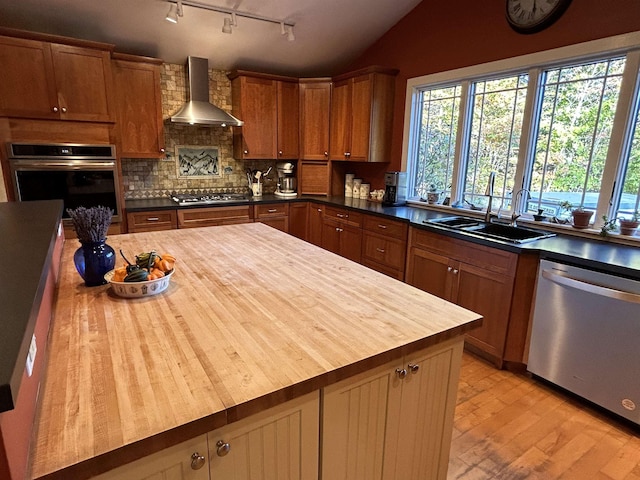 kitchen with butcher block countertops, sink, appliances with stainless steel finishes, backsplash, and wall chimney exhaust hood