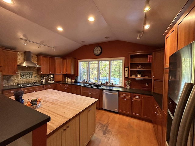 kitchen with appliances with stainless steel finishes, wood counters, lofted ceiling, sink, and wall chimney range hood