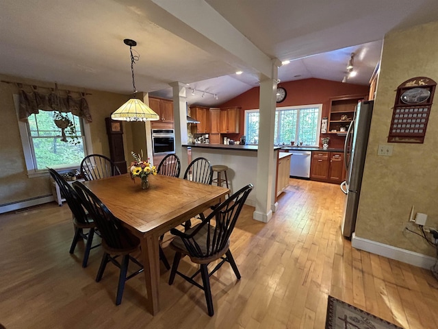 dining area featuring vaulted ceiling, rail lighting, a wealth of natural light, and light hardwood / wood-style flooring