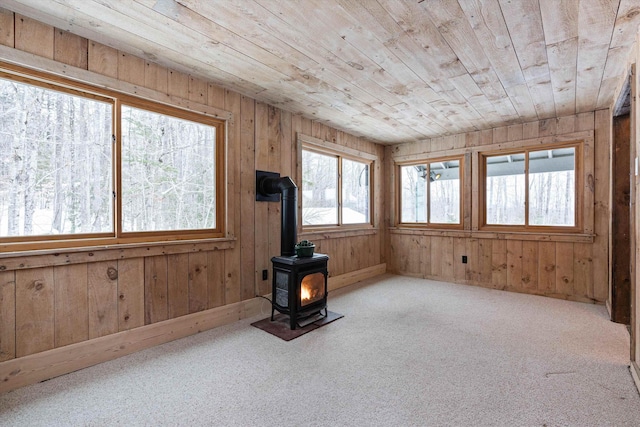 interior space with a wood stove, light colored carpet, wooden ceiling, and wooden walls