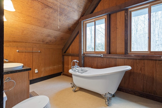 bathroom featuring wooden walls, vanity, a bath, vaulted ceiling, and toilet