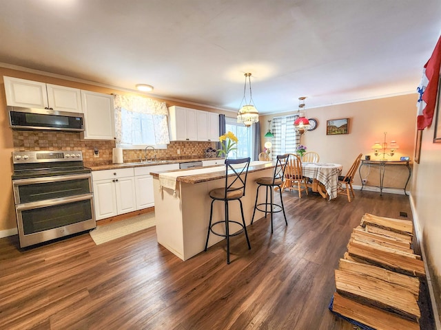 kitchen with appliances with stainless steel finishes, white cabinets, hanging light fixtures, ornamental molding, and a center island