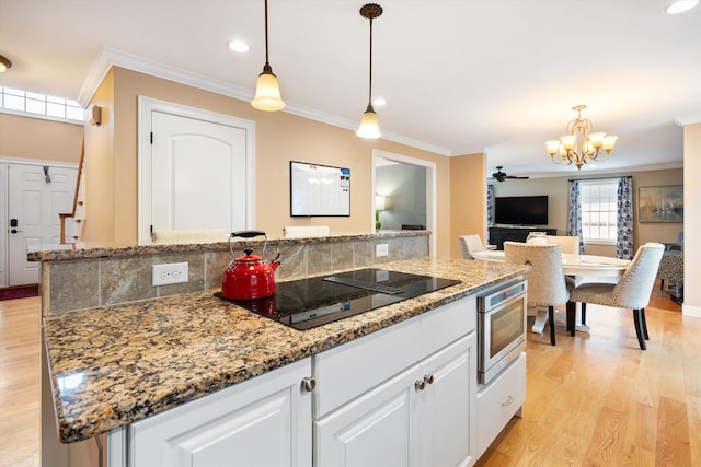 kitchen with a kitchen island, stainless steel microwave, white cabinets, and decorative light fixtures