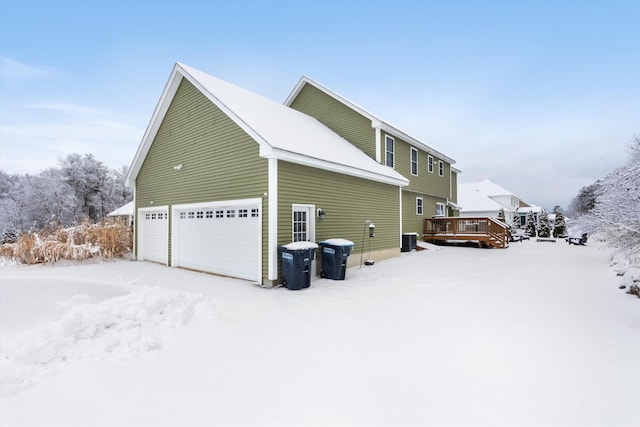 snow covered property featuring central AC, a garage, and a deck