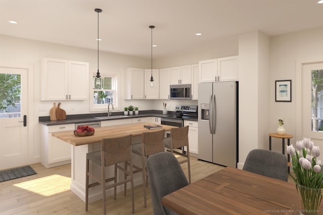 kitchen with appliances with stainless steel finishes, pendant lighting, sink, white cabinets, and light hardwood / wood-style flooring