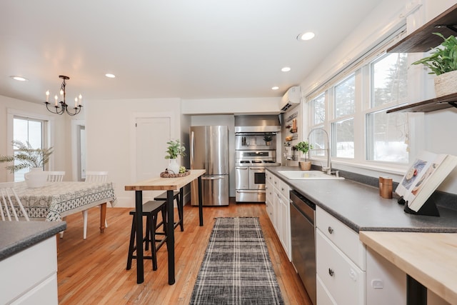 kitchen featuring sink, white cabinetry, a wall mounted air conditioner, hanging light fixtures, and stainless steel appliances