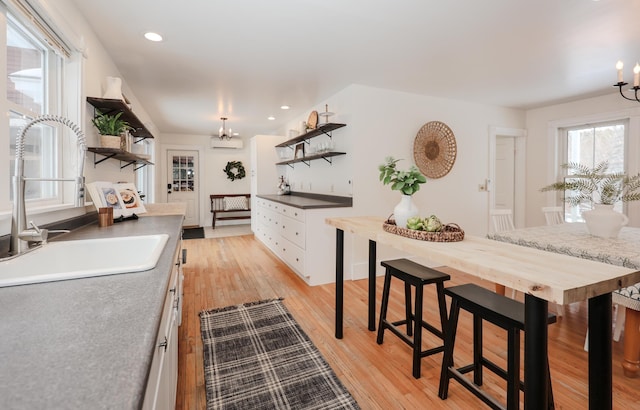 kitchen with sink, light hardwood / wood-style flooring, an inviting chandelier, white cabinetry, and a wall mounted AC