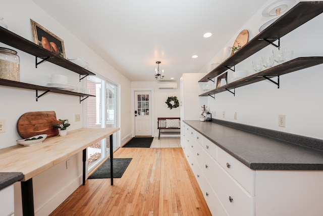 kitchen featuring light hardwood / wood-style flooring, wooden counters, a wall mounted AC, a notable chandelier, and white cabinets