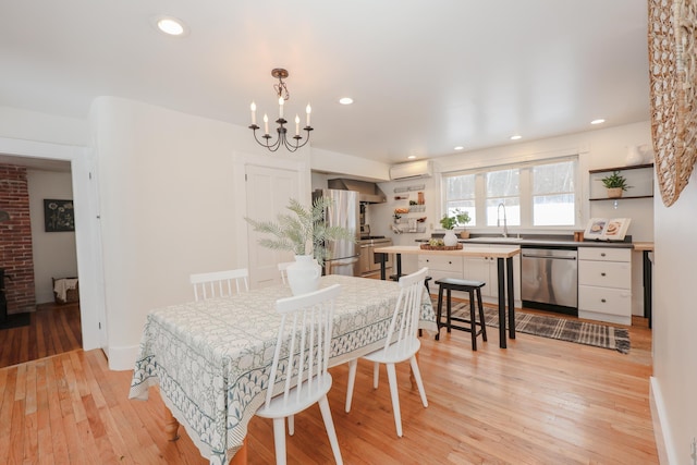 dining space with a wall unit AC, sink, a notable chandelier, and light wood-type flooring