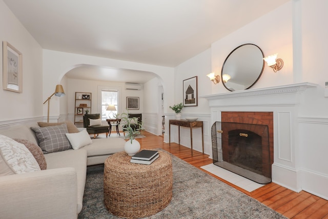 living room featuring a brick fireplace, a wall mounted AC, and light hardwood / wood-style floors