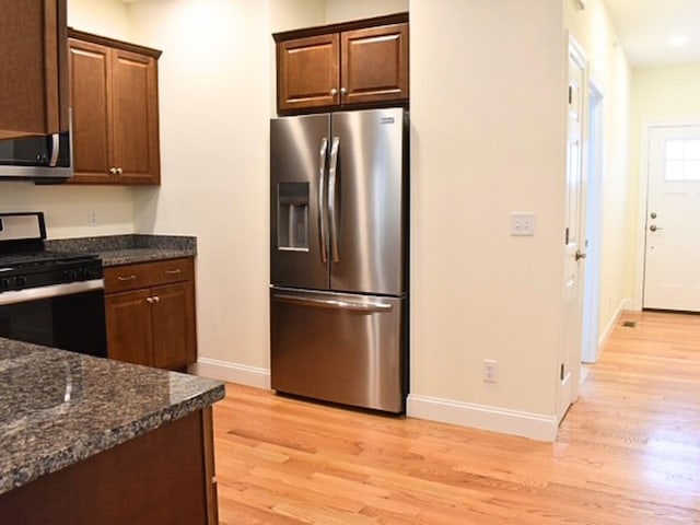 kitchen with light hardwood / wood-style flooring, stainless steel appliances, and dark stone counters