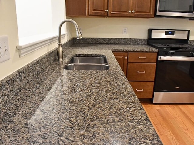 kitchen featuring light wood-type flooring, appliances with stainless steel finishes, sink, and dark stone countertops