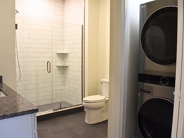 bathroom with toilet, a shower with shower door, vanity, stacked washing maching and dryer, and tile patterned flooring