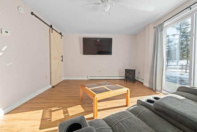 living room featuring light hardwood / wood-style flooring, ceiling fan, a baseboard heating unit, a barn door, and a wood stove