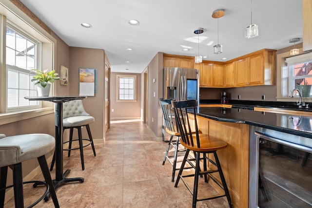 kitchen with sink, stainless steel fridge, hanging light fixtures, a kitchen breakfast bar, and beverage cooler