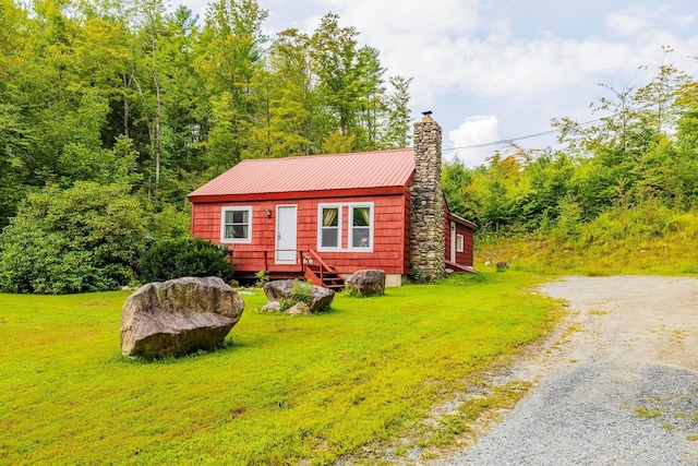 view of front of property featuring driveway, metal roof, a chimney, and a front lawn