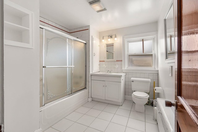 full bathroom featuring combined bath / shower with glass door, tile walls, tile patterned flooring, vanity, and toilet