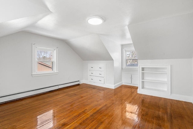 additional living space with wood-type flooring, vaulted ceiling, baseboard heating, and built in shelves