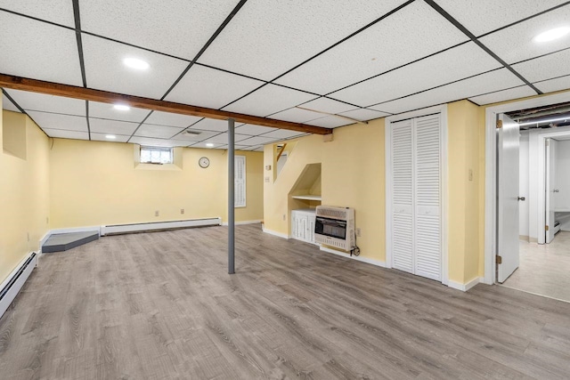 basement featuring heating unit, a baseboard heating unit, light hardwood / wood-style flooring, and a paneled ceiling