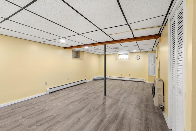 basement with hardwood / wood-style floors, a paneled ceiling, a wall unit AC, and baseboard heating