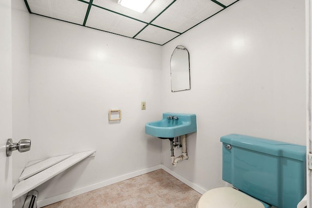 bathroom featuring baseboard heating, toilet, sink, and a drop ceiling