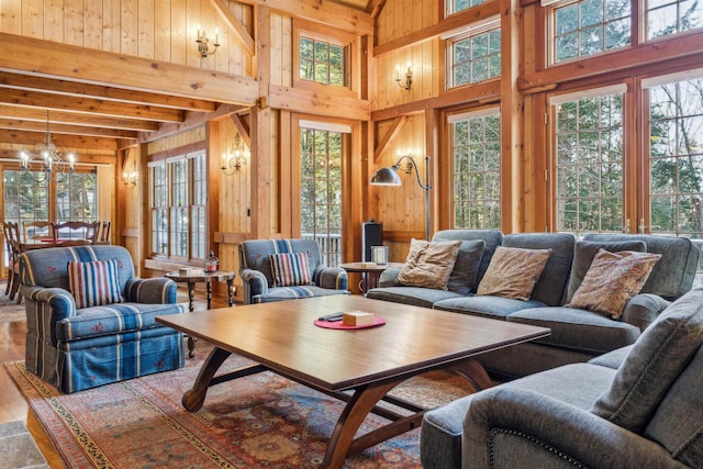 living room with an inviting chandelier, plenty of natural light, wooden walls, and beam ceiling