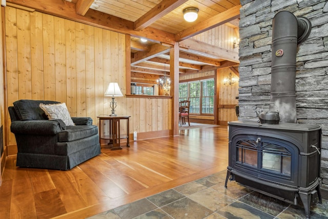 sitting room featuring an inviting chandelier, wooden walls, a wood stove, wood ceiling, and beam ceiling