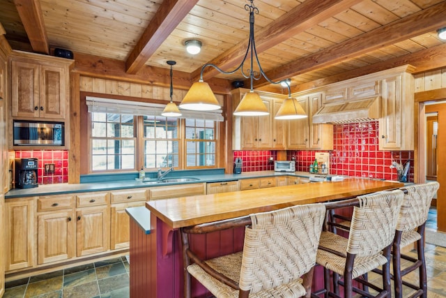 kitchen featuring stainless steel microwave, sink, butcher block counters, hanging light fixtures, and custom range hood