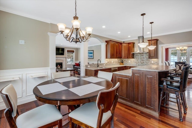 dining room with decorative columns, crown molding, dark wood-type flooring, and an inviting chandelier