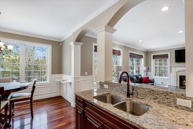 kitchen featuring ornate columns, sink, dark hardwood / wood-style flooring, a high end fireplace, and light stone counters