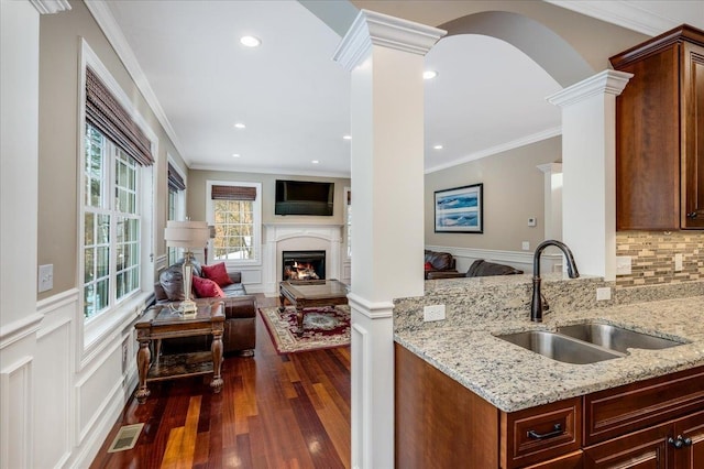 kitchen featuring decorative columns, sink, decorative backsplash, light stone counters, and dark wood-type flooring