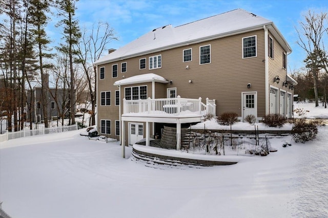 snow covered rear of property with a garage and a deck