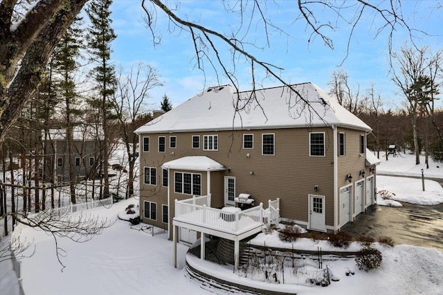 snow covered house with a garage and a wooden deck