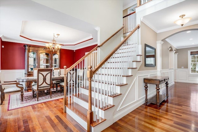 staircase with crown molding, a notable chandelier, hardwood / wood-style flooring, and decorative columns