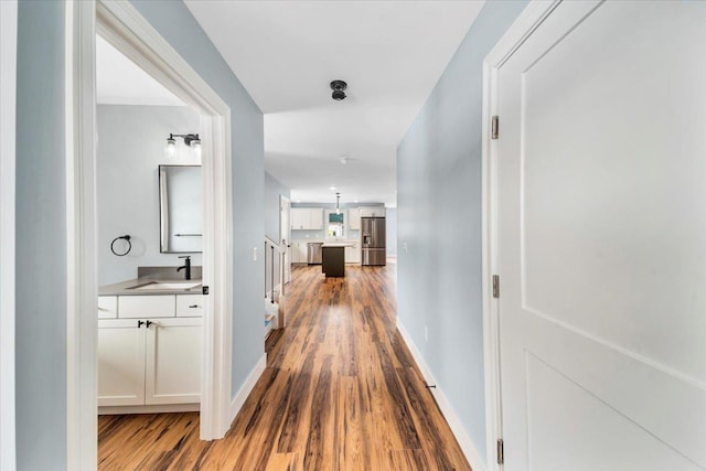 corridor with dark wood-type flooring, baseboards, and a sink