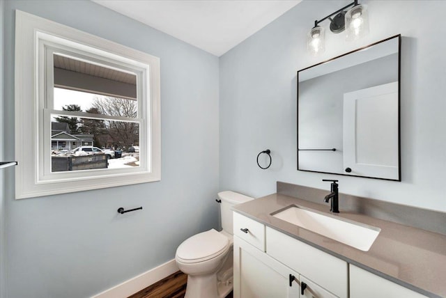 half bathroom featuring toilet, vanity, baseboards, and wood finished floors