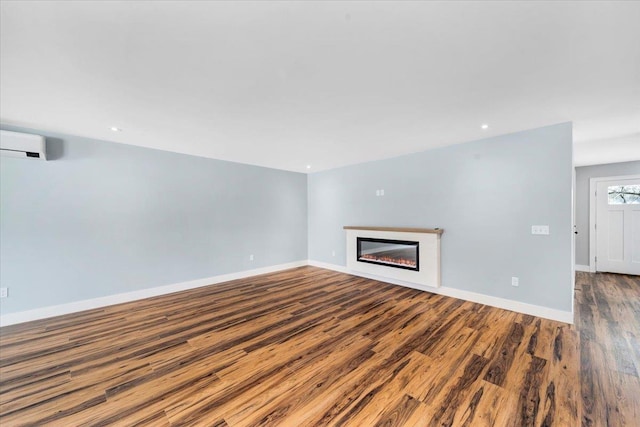 unfurnished living room with a wall mounted air conditioner, baseboards, wood finished floors, and a glass covered fireplace