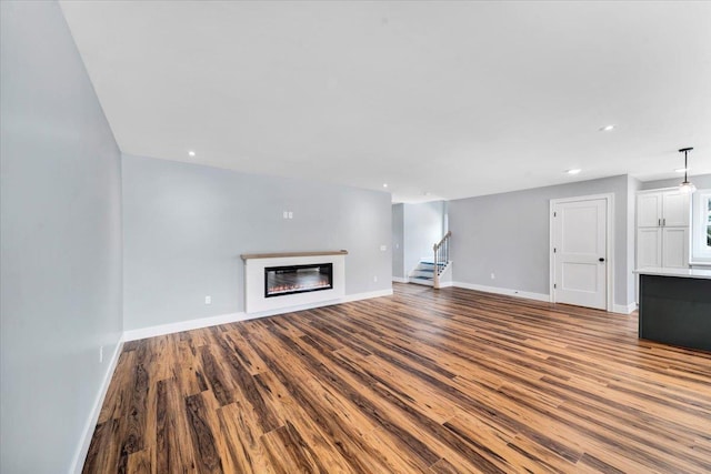 unfurnished living room featuring a glass covered fireplace, stairway, wood finished floors, and baseboards