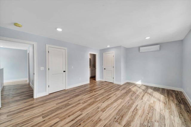 unfurnished room with light wood-type flooring, baseboards, and an AC wall unit