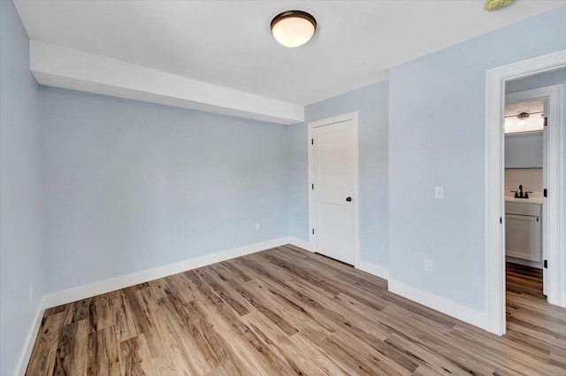 unfurnished bedroom featuring light wood finished floors, a closet, baseboards, and a sink