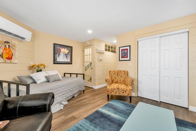 bedroom with hardwood / wood-style floors, a wall mounted air conditioner, wooden walls, and a closet