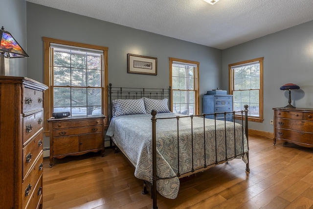 bedroom featuring hardwood / wood-style floors, a textured ceiling, and baseboard heating