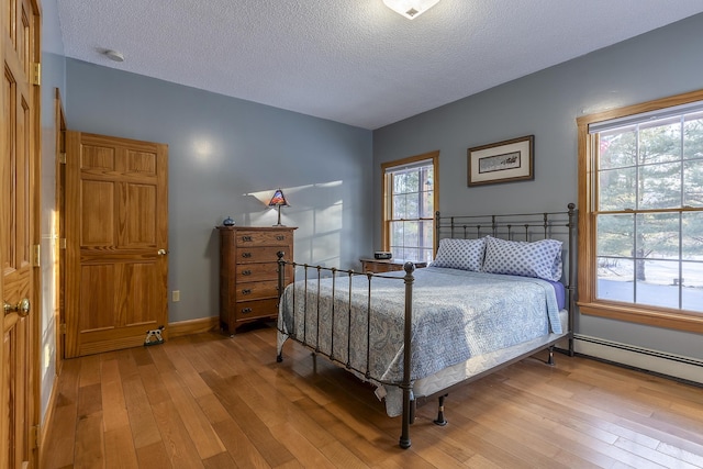 bedroom with wood-type flooring, a textured ceiling, and a baseboard heating unit